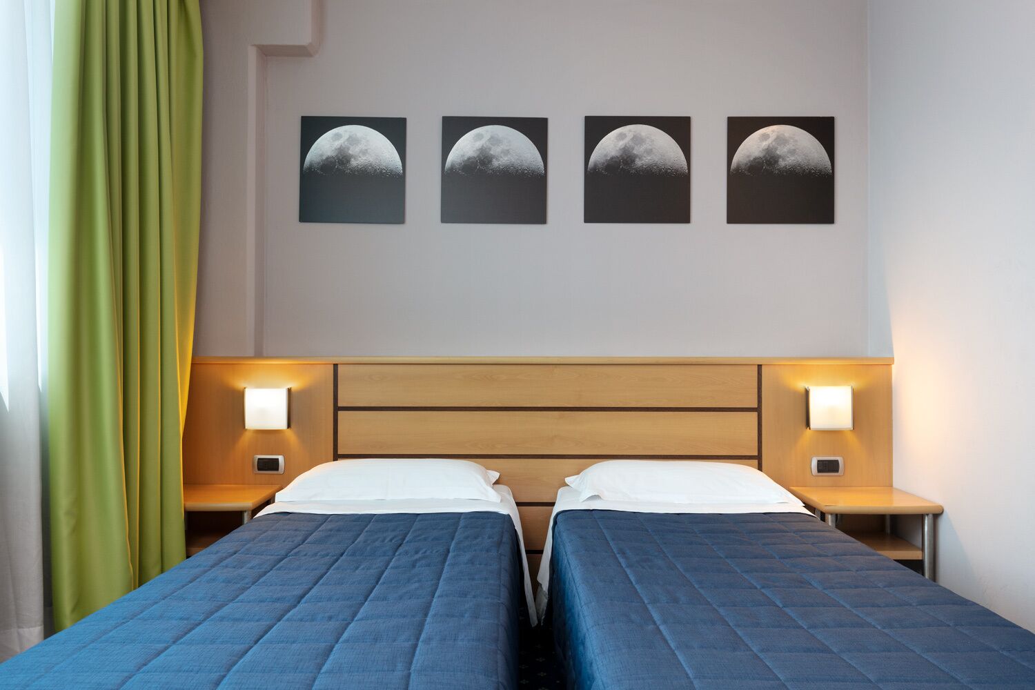 Ein Hotelzimmer mit zwei Betten, einem Holz-Kopfteil, Nachttischlampen und vier Bildern der Mondphasen an der Wand.