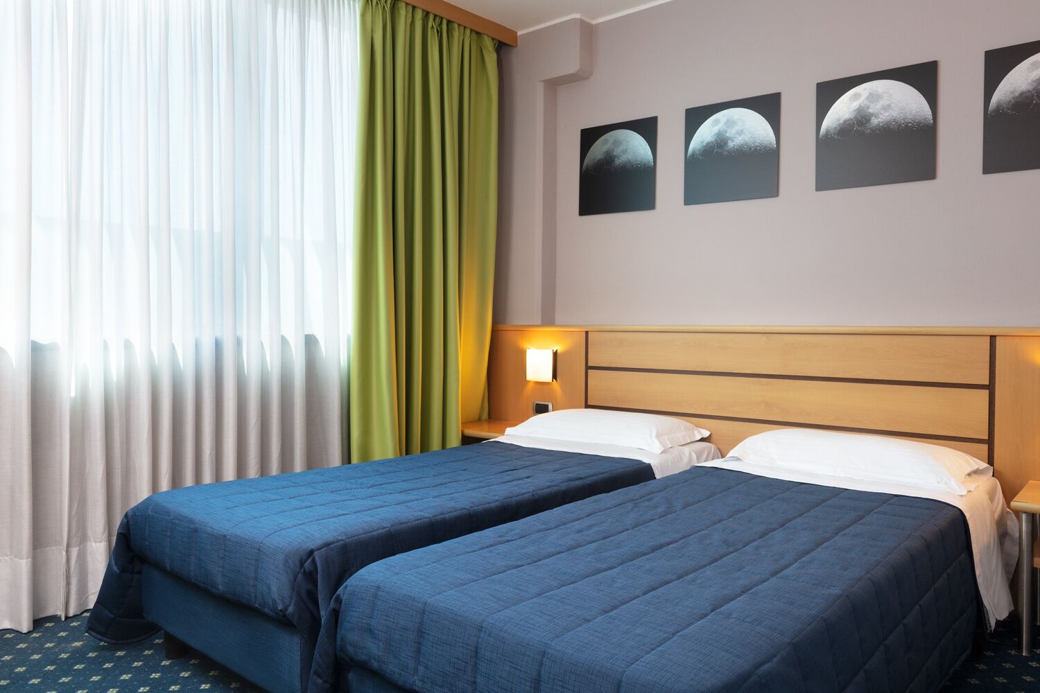 Habitación de hotel con dos camas, una cortina verde y tres imágenes de las fases lunares en la pared.