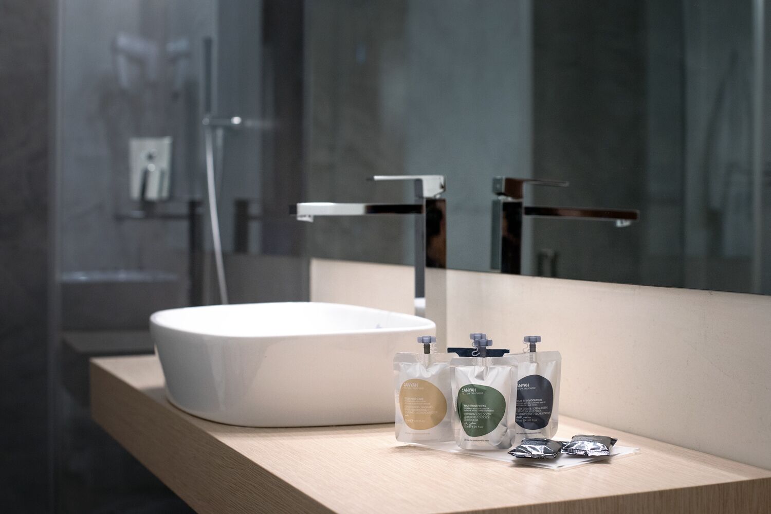 Ein modernes Badezimmer mit einem großen weißen Waschbecken, einem Spiegel und drei Pflegeprodukten auf einer Holzauskleidung.
