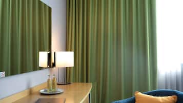 A hotel room with a wooden desk, a laptop, a lamp, and a chair with a cushion.