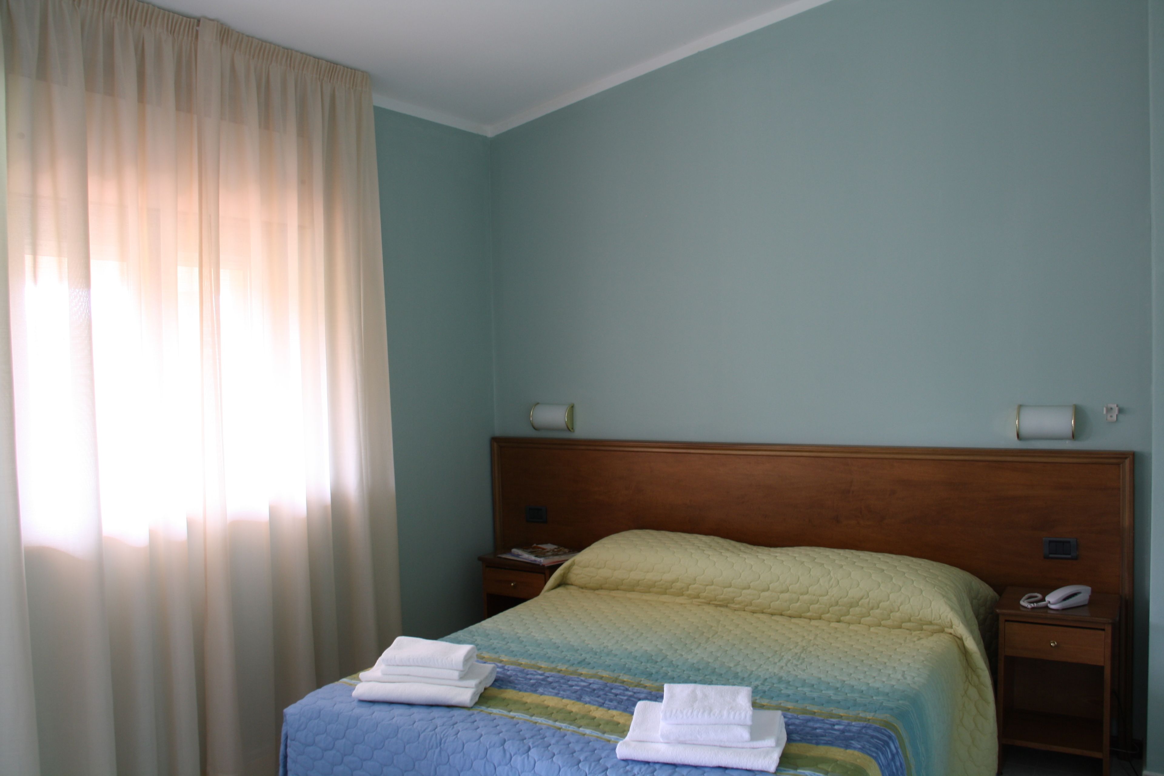 A hotel room with a bed, a nightstand with a telephone, and a window with curtains.