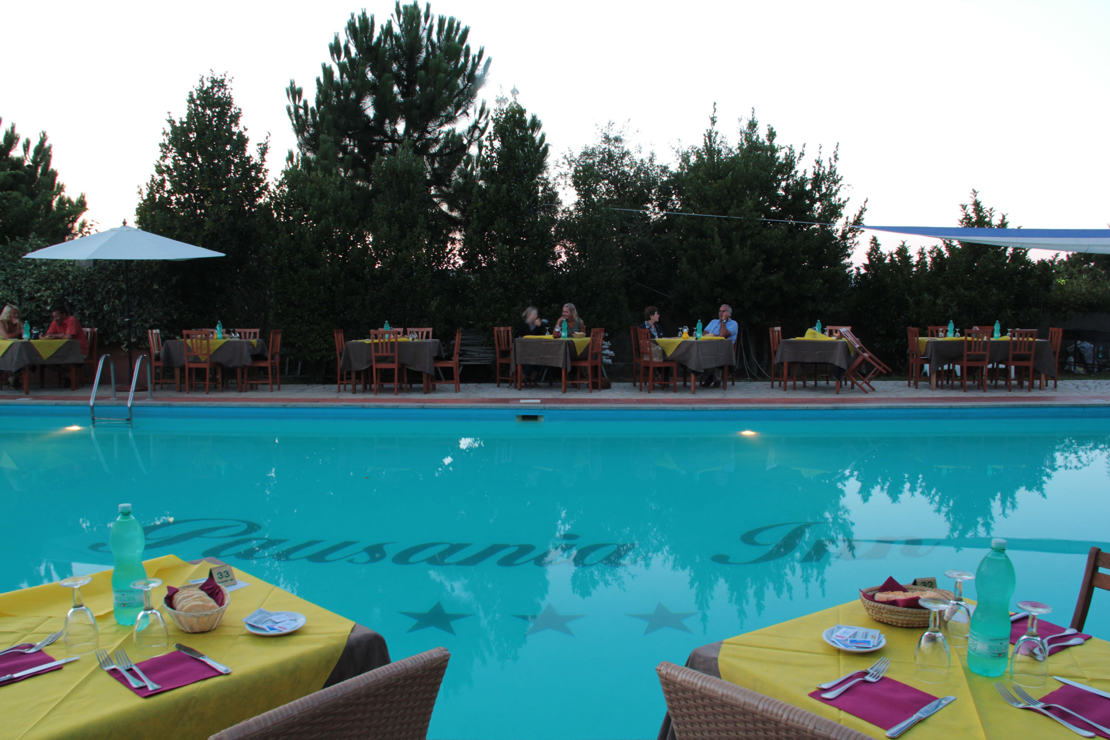 Un espace de restauration en plein air avec des tables pour deux, donnant sur une piscine où l’on peut lire le mot « Pousada » sur la surface de l’eau.