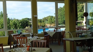 A restaurant with large windows overlooking a pool and greenery. Tables are set with wine glasses and cutlery. - Pausania Inn (Tempio Pausania)