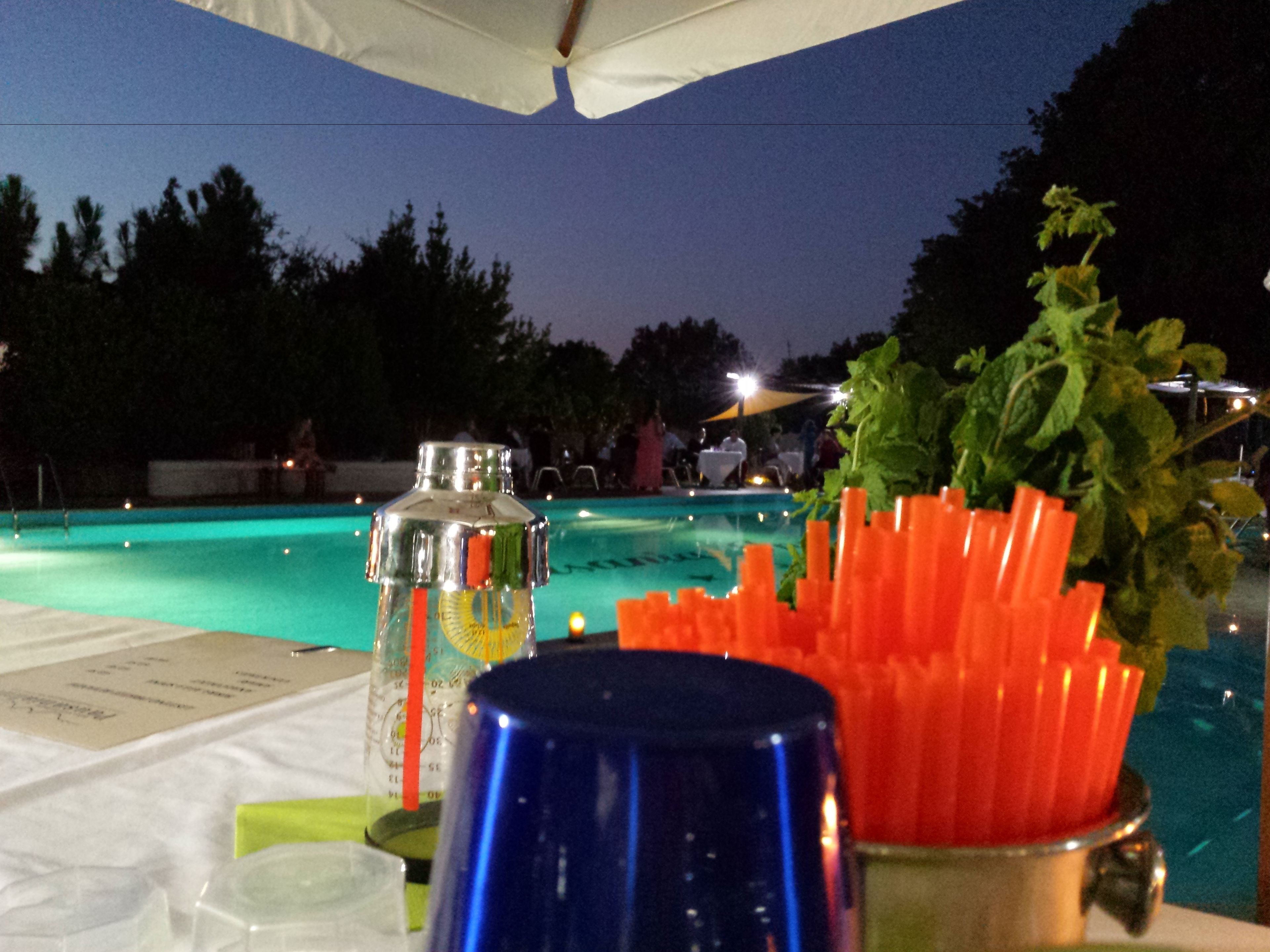 A poolside table with a bottle, a blue cup, and a container of carrot sticks.