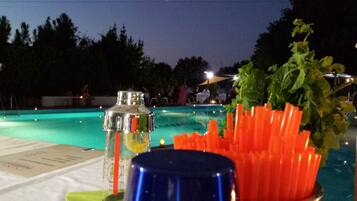 A poolside table with a bottle, a blue cup, and a container of carrot sticks.