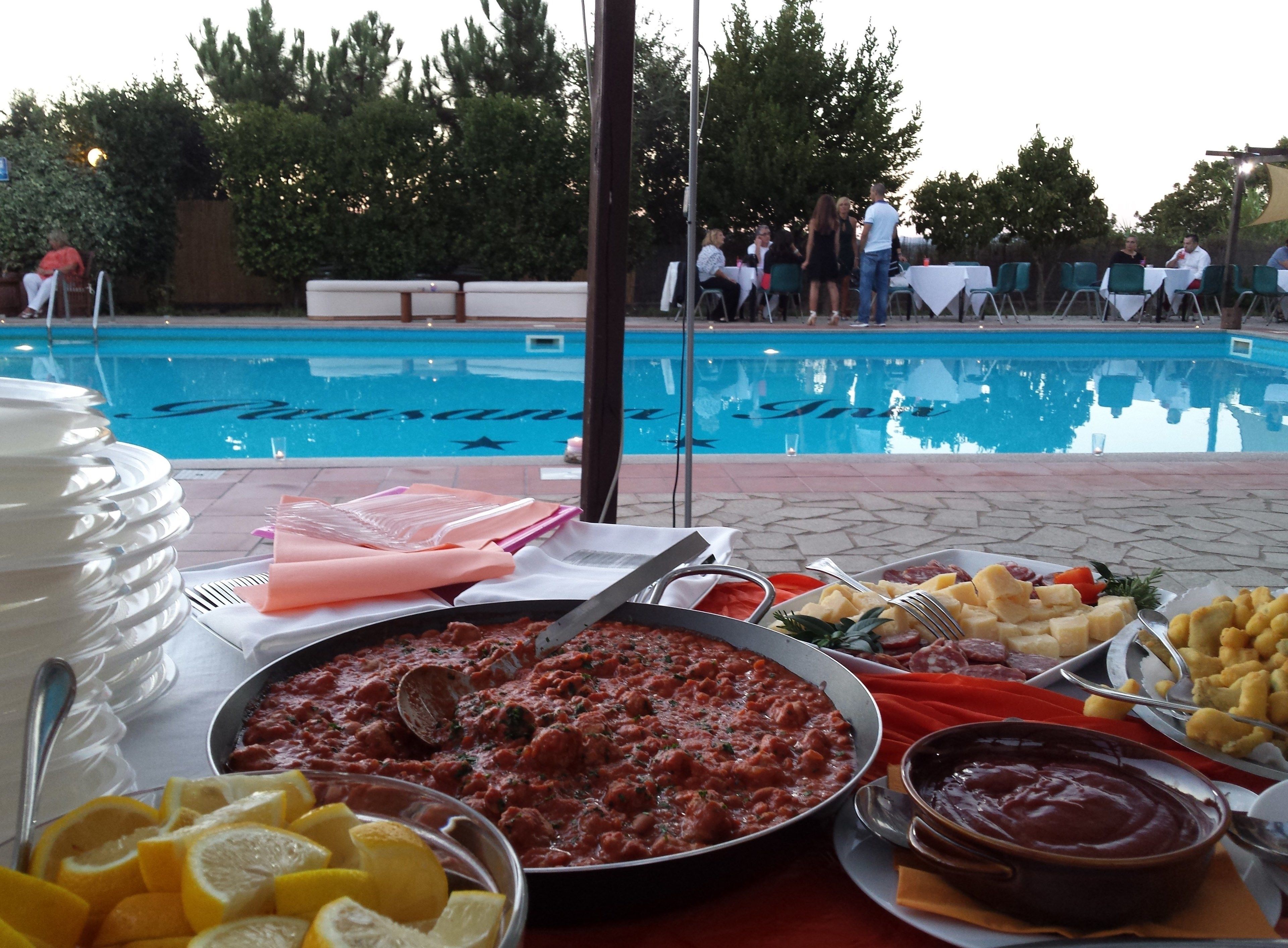 Ein Büfett mit verschiedenen Speisen, im Hintergrund ein Pool und Gäste, die essen.