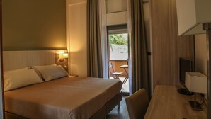 A hotel room with a bed, a desk, a chair, a TV, and a balcony with a table and chairs. - Pausania Inn (Tempio Pausania)