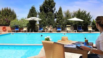 A swimming pool with lounge chairs and umbrellas, surrounded by trees and a clear sky.