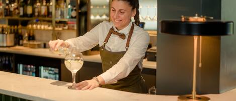 A bartender at a bar counter with shelves of bottles in the background.