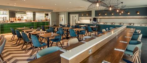 Een modern restaurant met een lange toonbank, blauwe gestoffeerde stoelen en een bar met groene tegels.