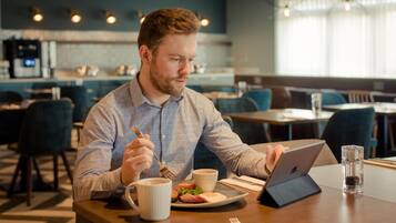 A man sitting at a table in a modern dining area with a laptop, a cup of coffee, and a plate of food.