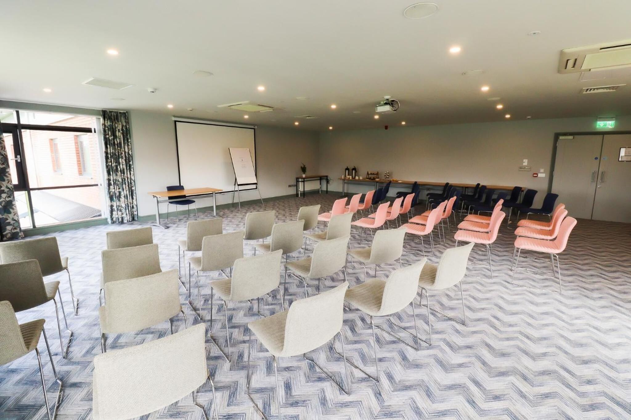 Une salle de conférence équipée d’un grand écran, d’un projecteur et de plusieurs rangées de chaises.