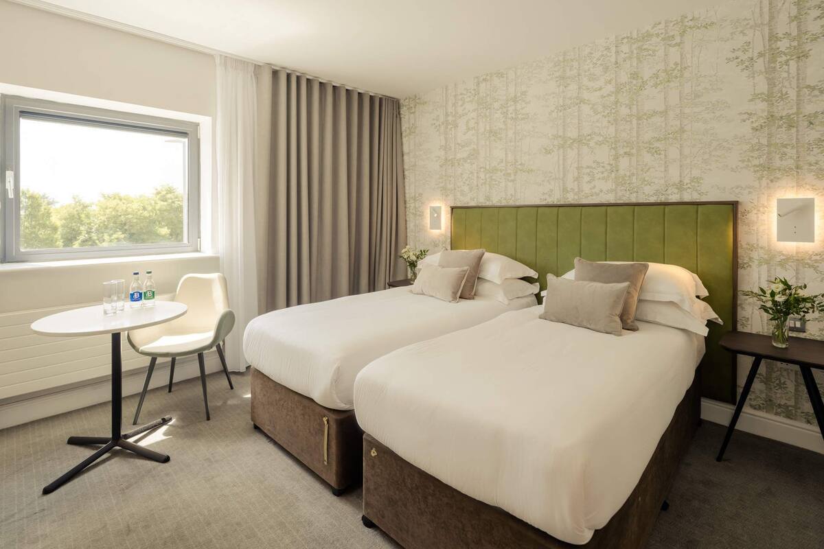 A hotel room with two beds, a small table, and a chair.