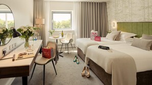Ein Hotelzimmer mit Bett, Schreibtisch, Stuhl, Tisch mit Blumenvase und einem fensterbepflanzten Fenster.