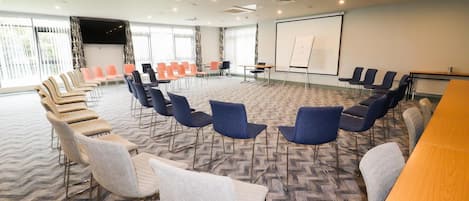Un salón de conferencias con una gran mesa, varias sillas, una pizarra y una pantalla de proyector.