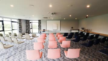 A conference room with rows of chairs, a projector screen, and a presentation area.