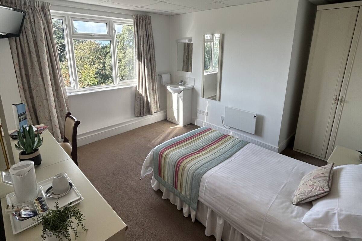 A hotel room with a bed, bedside table, and a window with curtains.