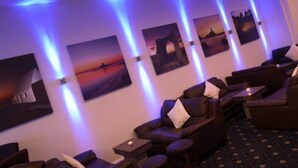 Een kamer met een rij massagestoelen, een klein tafeltje en kunstwerken aan de muur.