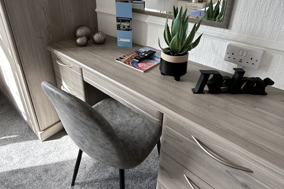 A modern bathroom with a wooden vanity, a large mirror, a potted plant, and a magazine on the counter.