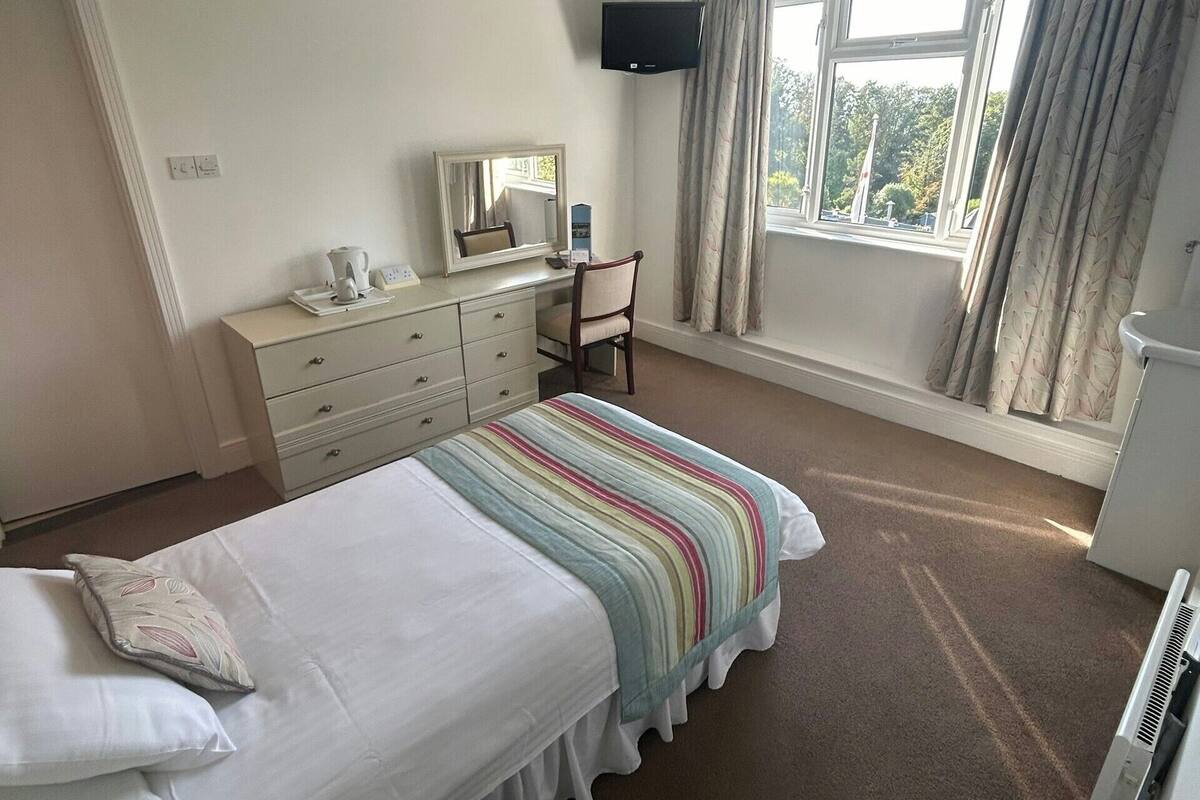 A hotel room with a bed, a desk, a chair, a TV, and a window with curtains.