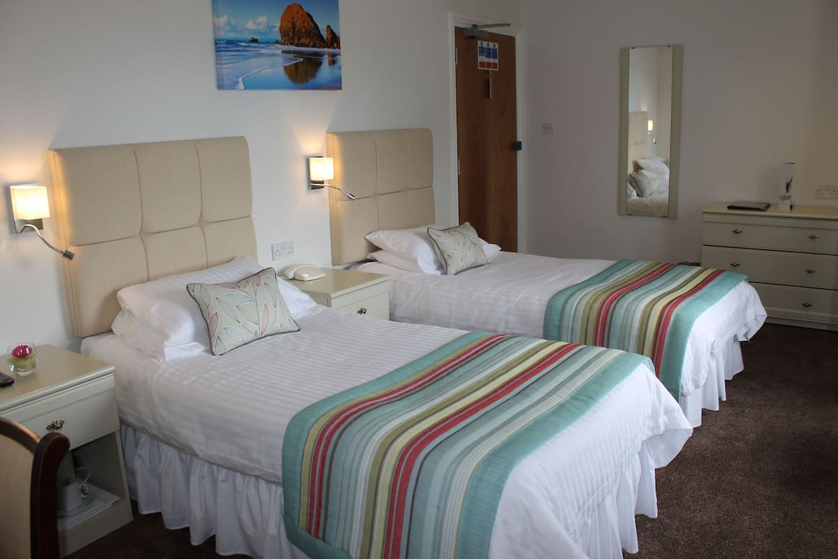 A hotel room with two beds, a nightstand with a lamp, a dresser, and a painting on the wall.