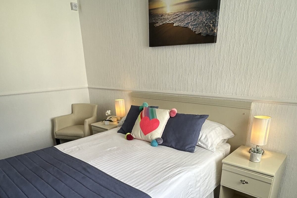 A hotel room with a bed, two bedside tables, a nightstand, a lamp, and a painting on the wall.