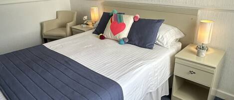 Une chambre d’hôtel avec un lit, deux tables de chevet, une petite table, une lampe et un tableau au mur.