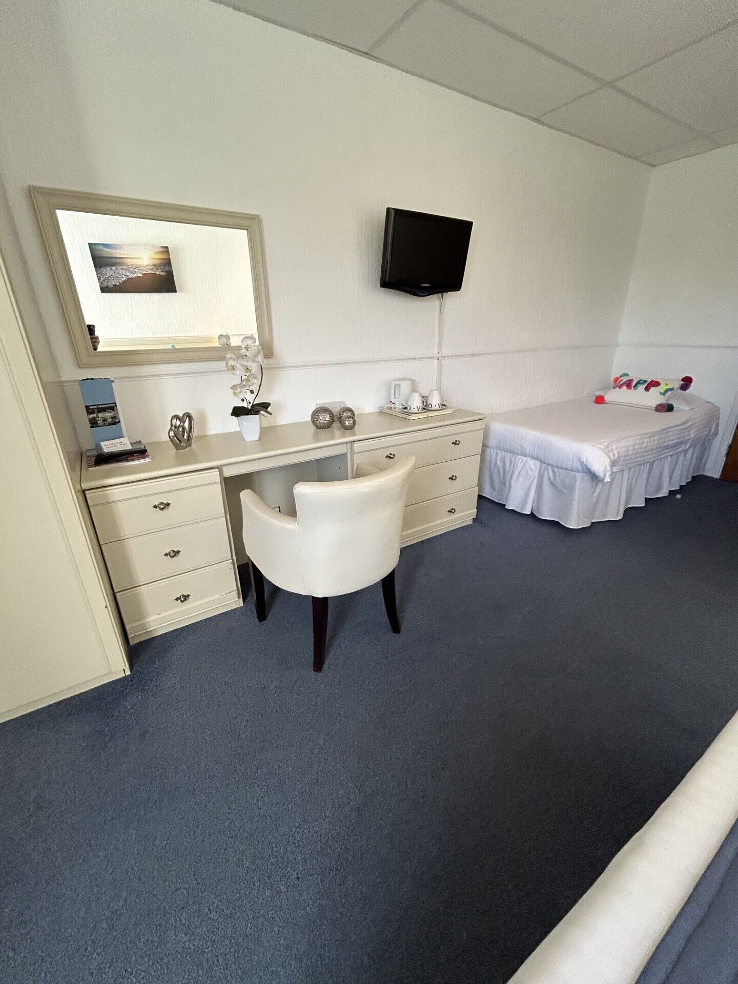 Ein Hotelzimmer mit Schreibtisch, Stuhl, Bett und einem an der Wand befestigten Fernseher.