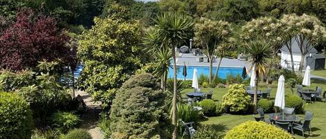 Un jardin aménagé avec une piscine, un espace salon extérieur et diverses espèces d’arbres et d’arbustes.