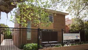 A brick building with a gated entrance, a bench outside, and a sign advertising a service. - Easystay Apartments (St. Kilda East)