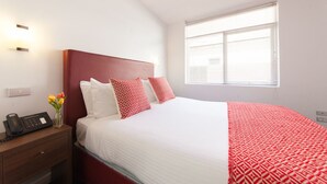 A hotel room with a large bed, a bedside table with a phone, and a window with blinds. - Easystay Apartments (St. Kilda East)