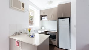 A modern kitchen with a central island, built-in microwave, oven, and refrigerator. - Easystay Apartments (St. Kilda East)