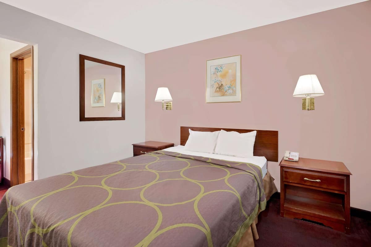 Habitación de hotel con una cama grande, dos mesitas de noche, una puerta y dos lámparas fijadas a la pared.