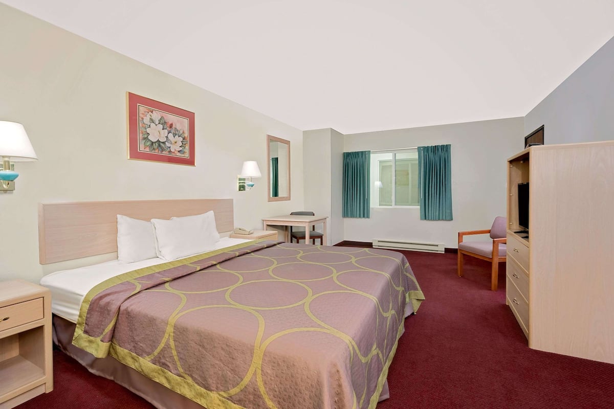 Una habitación de hotel con cama, escritorio, silla, armario y ventana con cortinas.