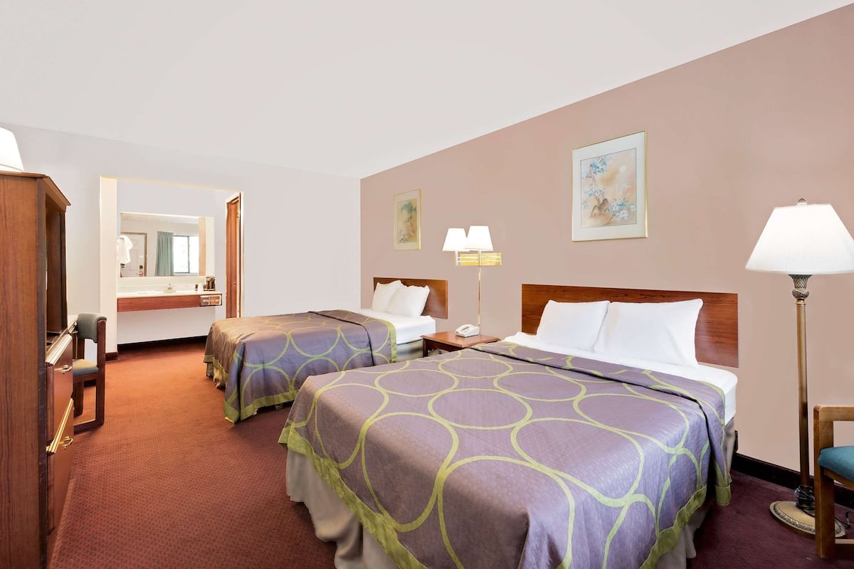 Habitación de hotel con dos camas, un escritorio, una silla, un espejo y un baño visible a través de una puerta abierta.