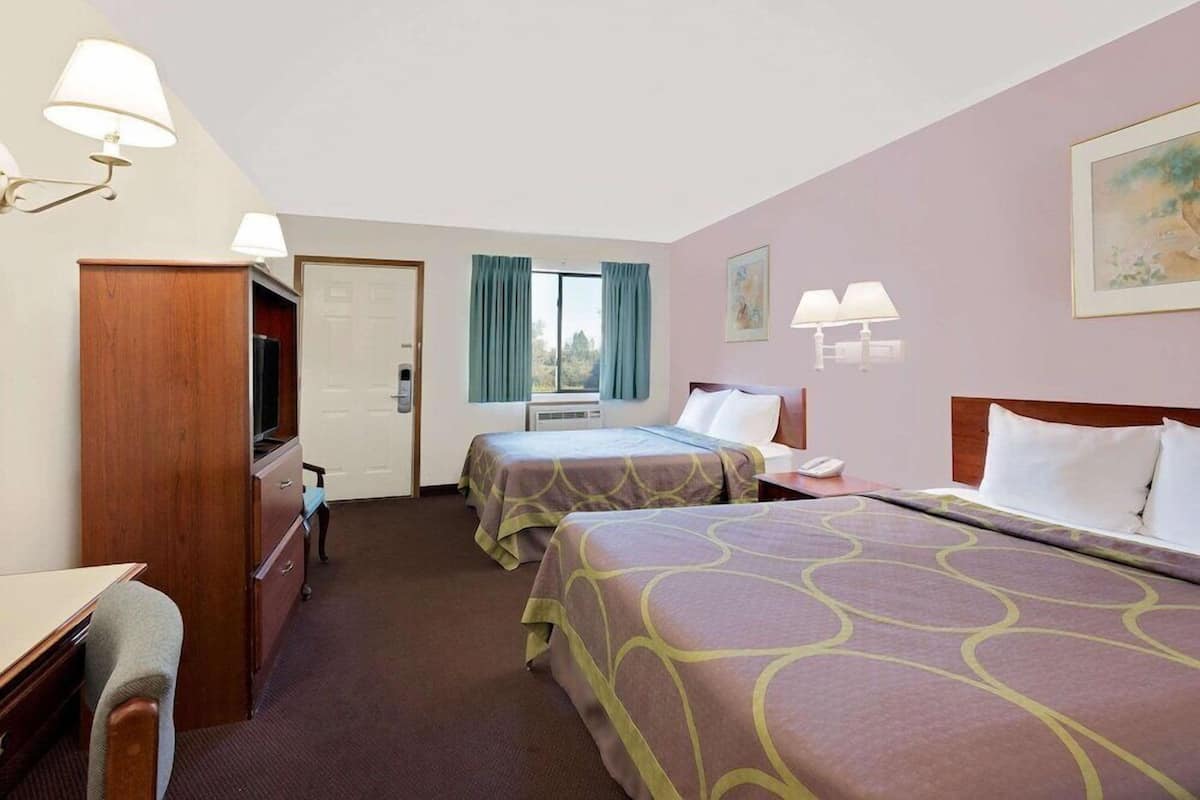 Una habitación de hotel con dos camas, un escritorio, un tocador, un televisor y una ventana con cortinas.