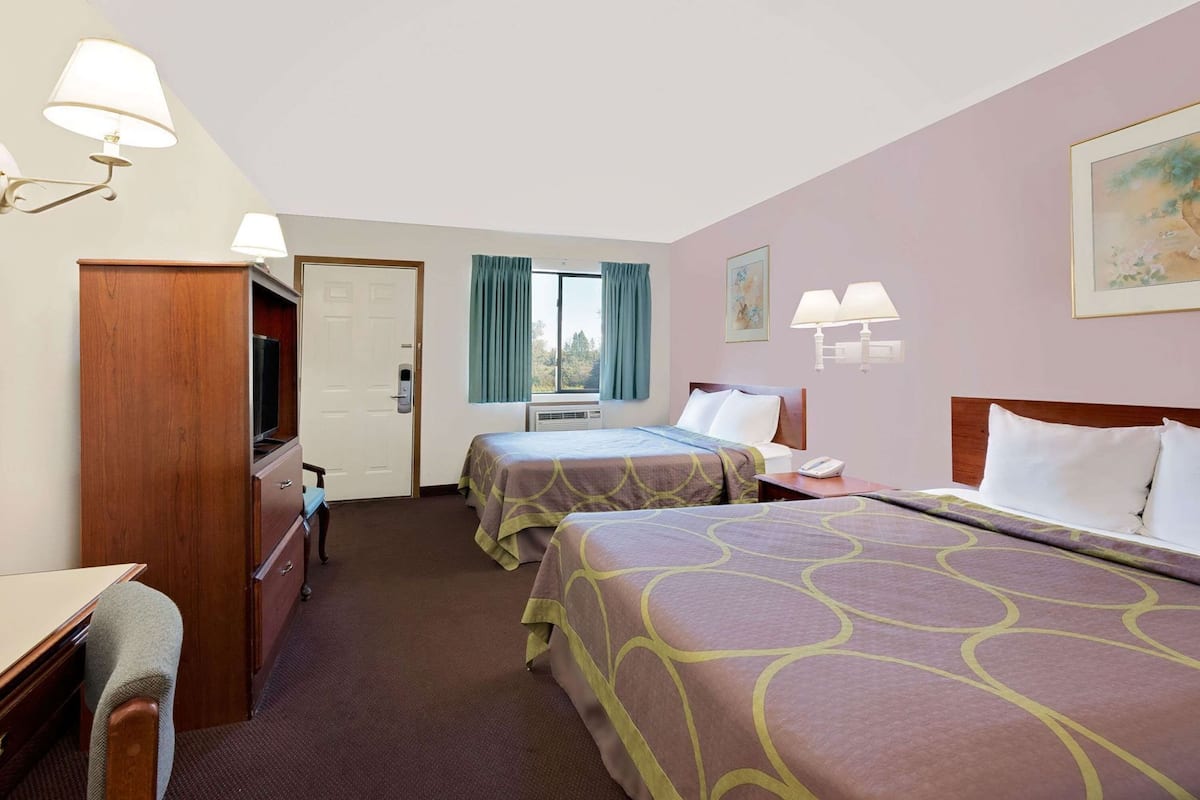 Habitación de hotel con dos camas, un escritorio, una silla, un televisor y una ventana con cortinas.