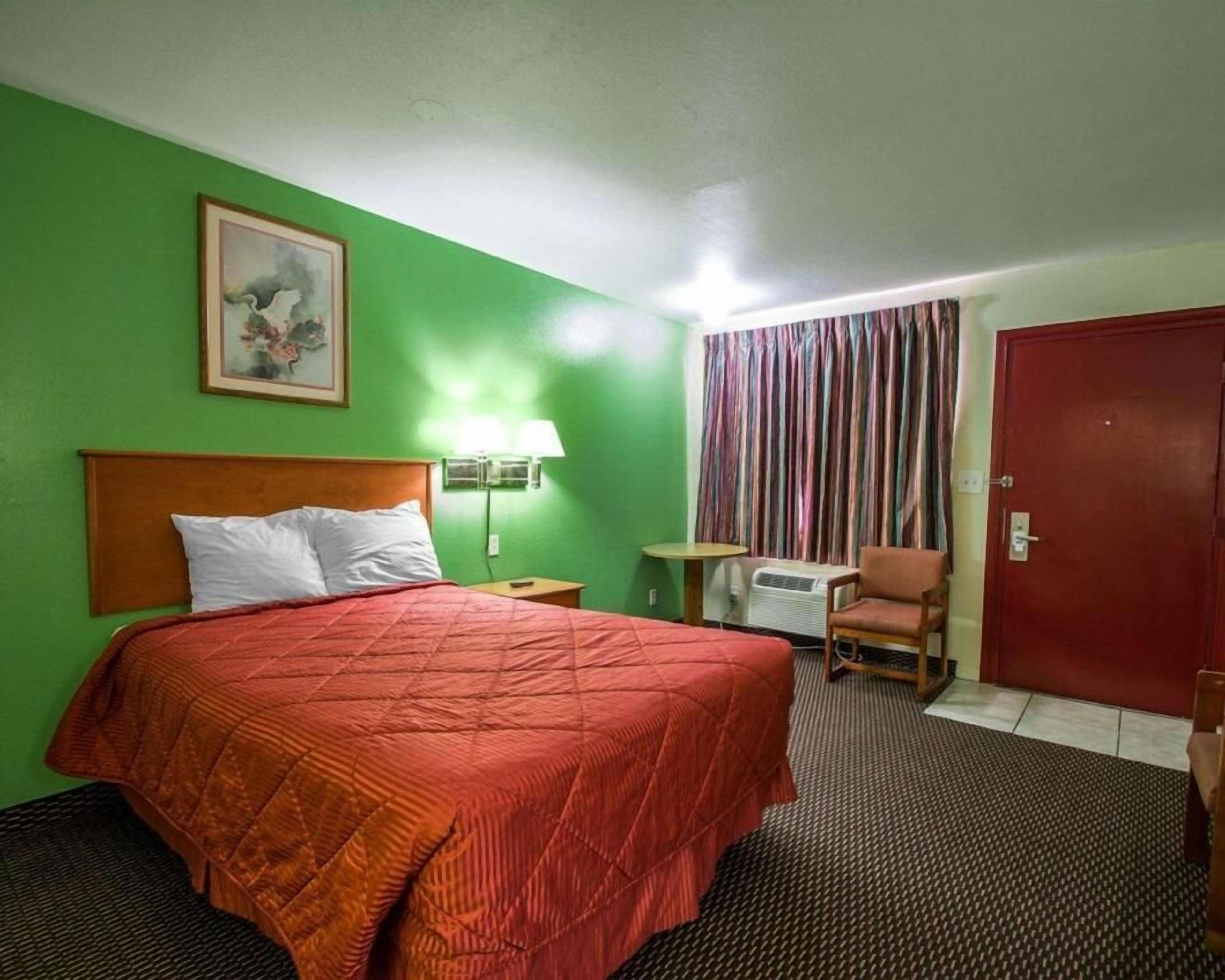 Une chambre d’hôtel avec un lit, une chaise, une table, une lampe et une porte.
