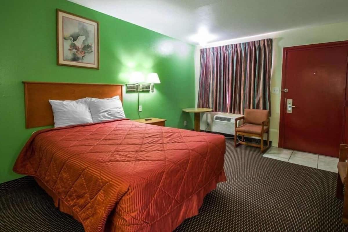 Une chambre d’hôtel avec un lit, une chaise, une table, une lampe et une porte.