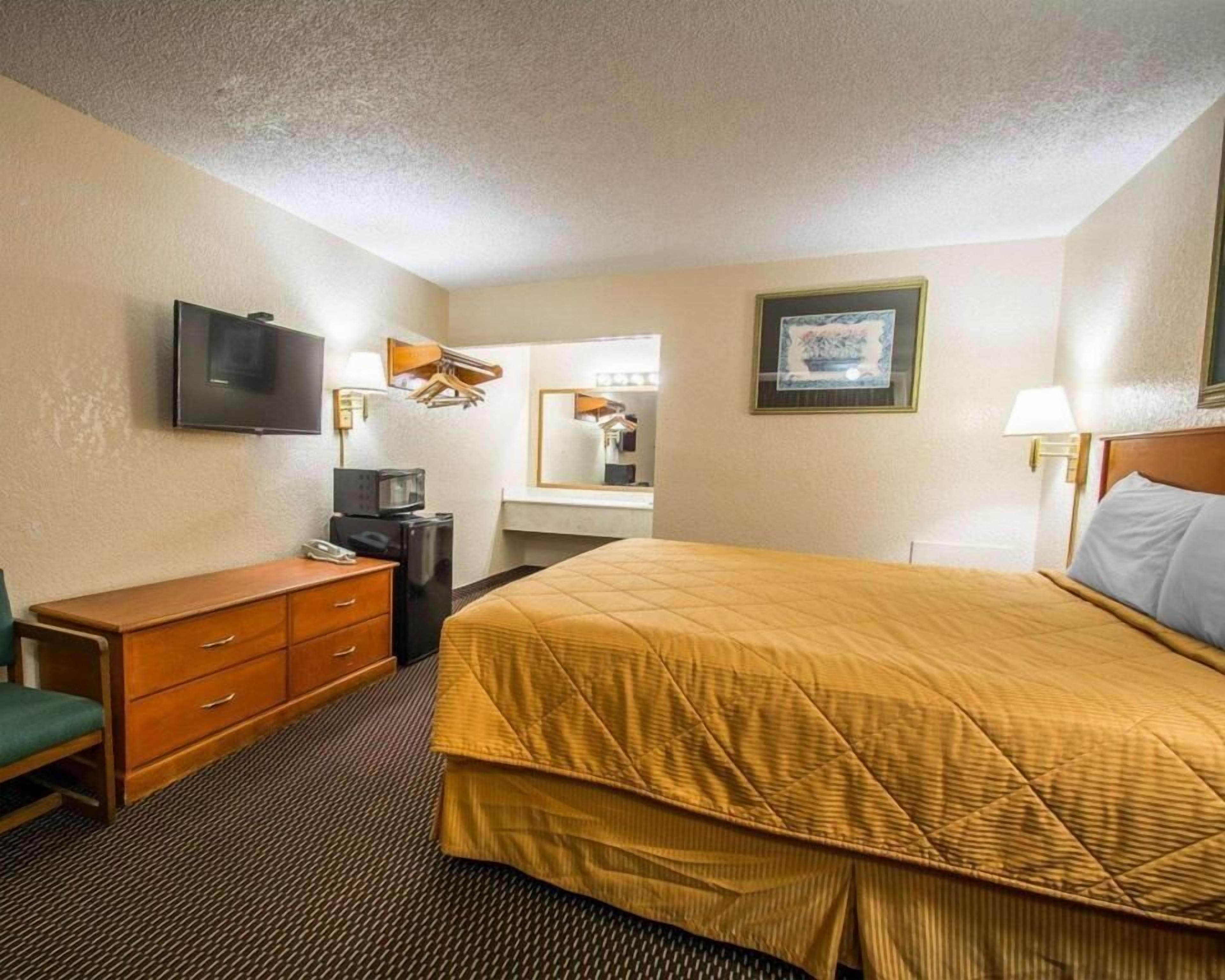 Une chambre d’hôtel avec un lit, un bureau avec un ordinateur, une télévision, un miroir et un tableau encadré au mur.