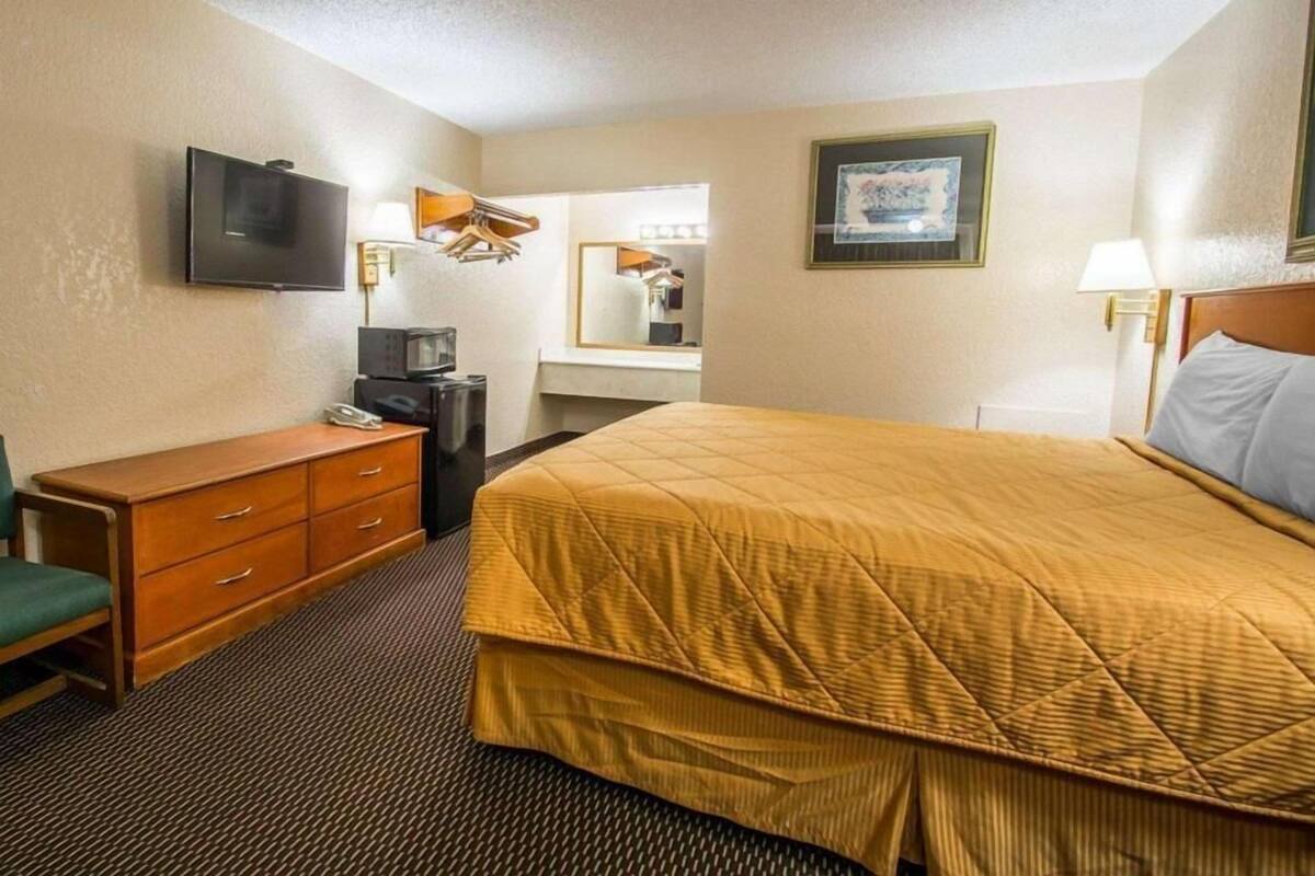 A hotel room with a bed, a desk with a computer, a television, a mirror, and a framed picture on the wall.