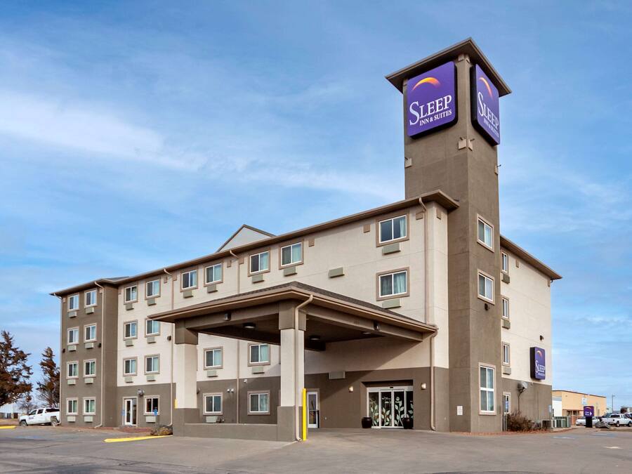 A multi-story hotel with a prominent Sleep Inn & Suites sign, a covered entrance, and a parking lot.