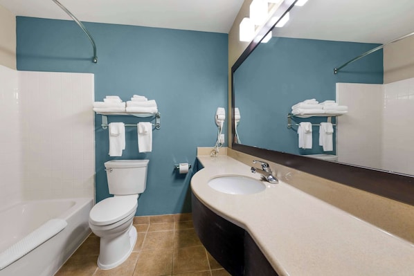 Casa de banho com sanita branca, lavatório e espelho. Há toalhas numa barra e um secador de cabelo na parede.