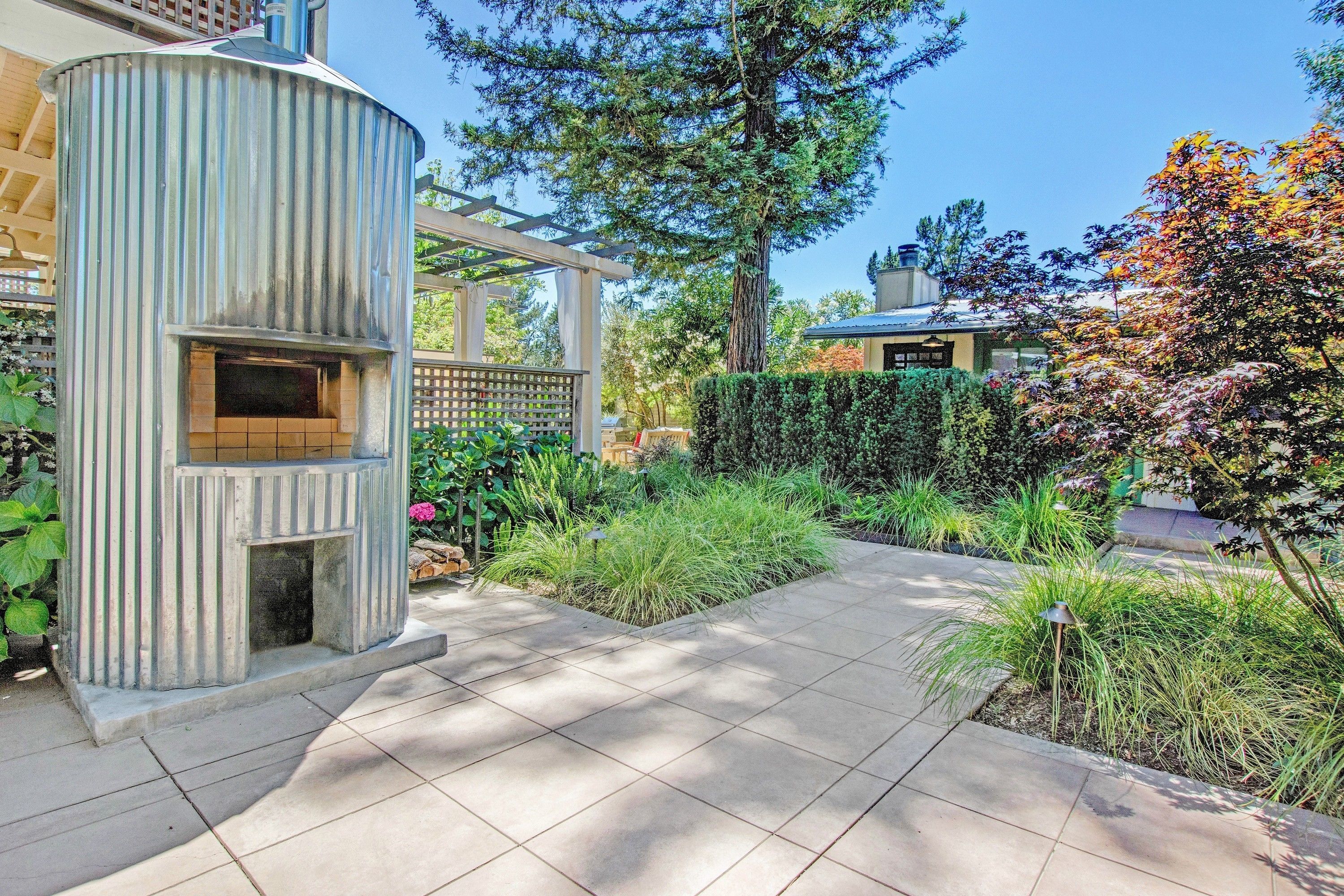 Un espace extérieur aménagé avec un barbecue en métal, une pergola et diverses plantes.