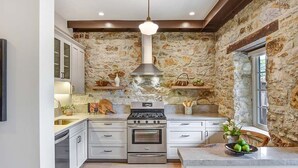 A kitchen with a stone wall, white cabinets, a stainless steel range, and a hanging light fixture.