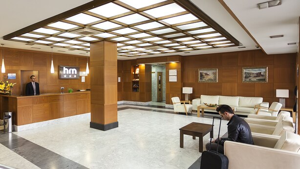 A hotel lobby with a reception desk, seating area, and a large skylight. - Hotel Manolo (Cartagena)