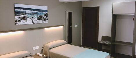 Habitación de hotel con dos camas, un cuadro de una playa, un armario y una mesita de noche con un teléfono.