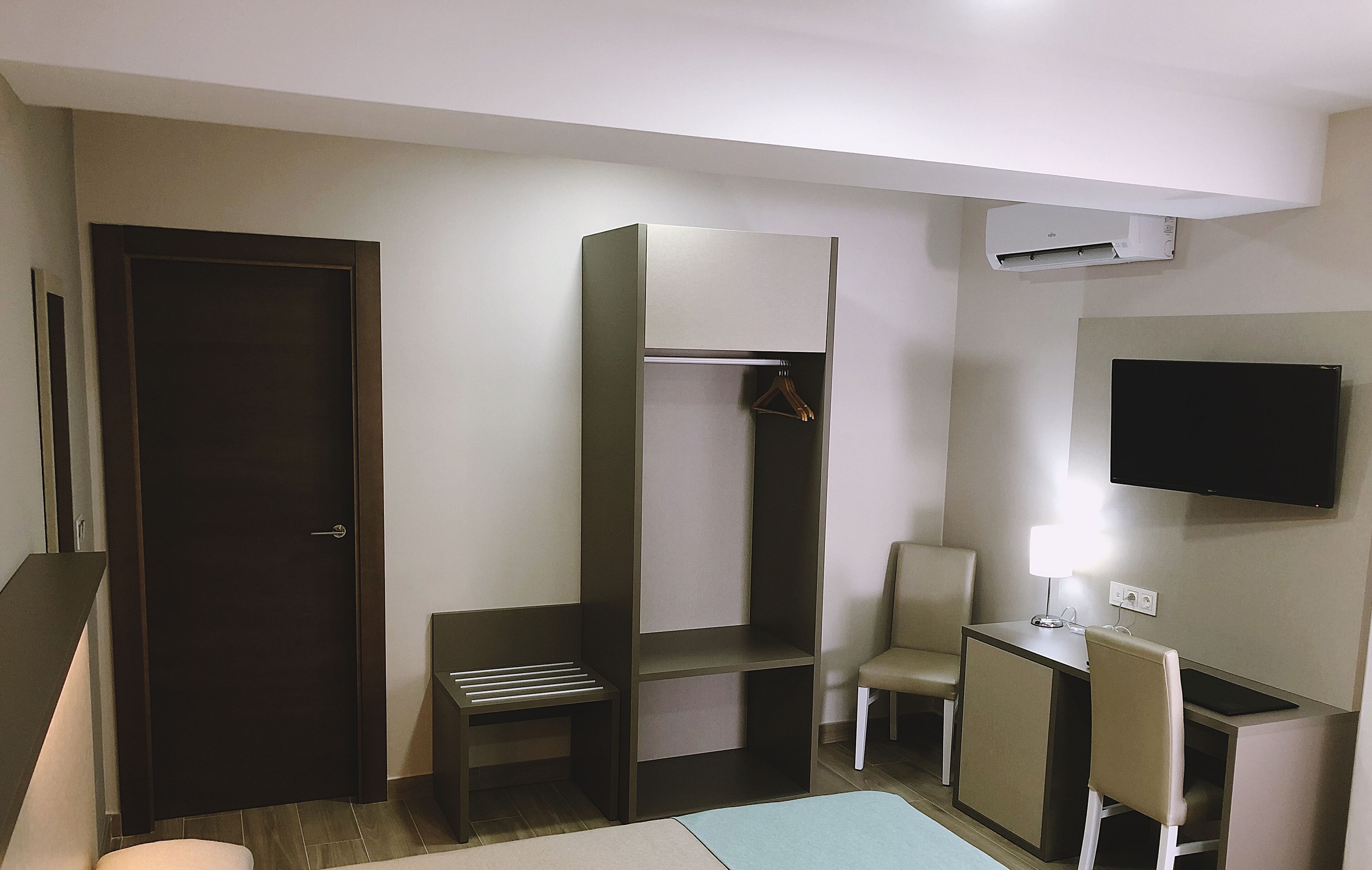 Habitación de hotel pequeña con cama, escritorio y silla, armario, televisor y aire acondicionado.