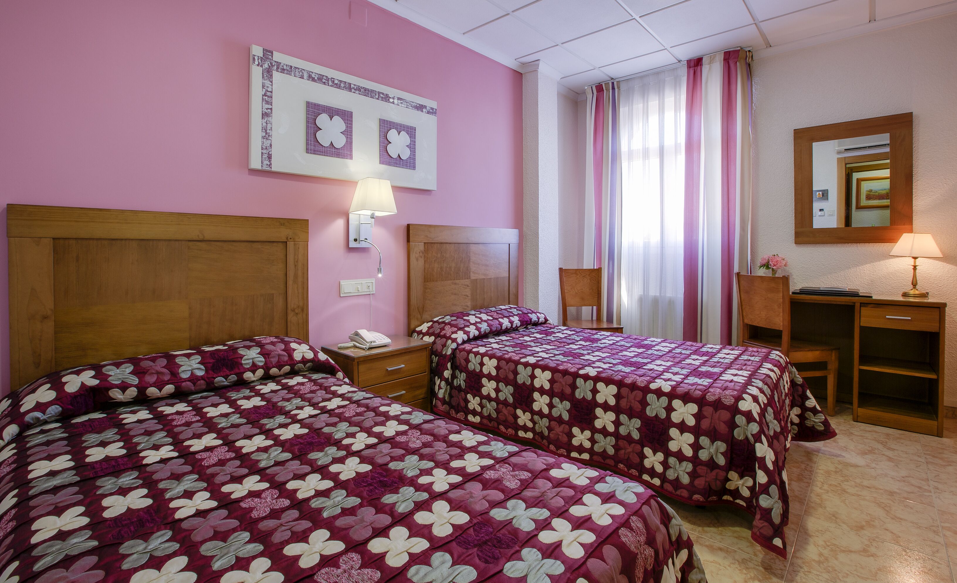 Ett hotellrum med två sängar, ett skrivbord, en stol, en lampa och en spegel.