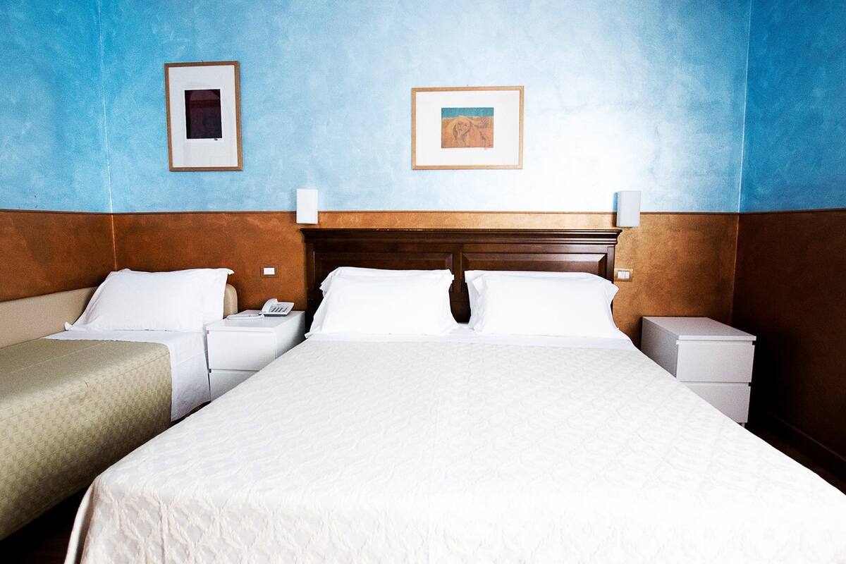 A hotel room with a large bed, two bedside tables, a nightstand, and two framed pictures on the wall.
